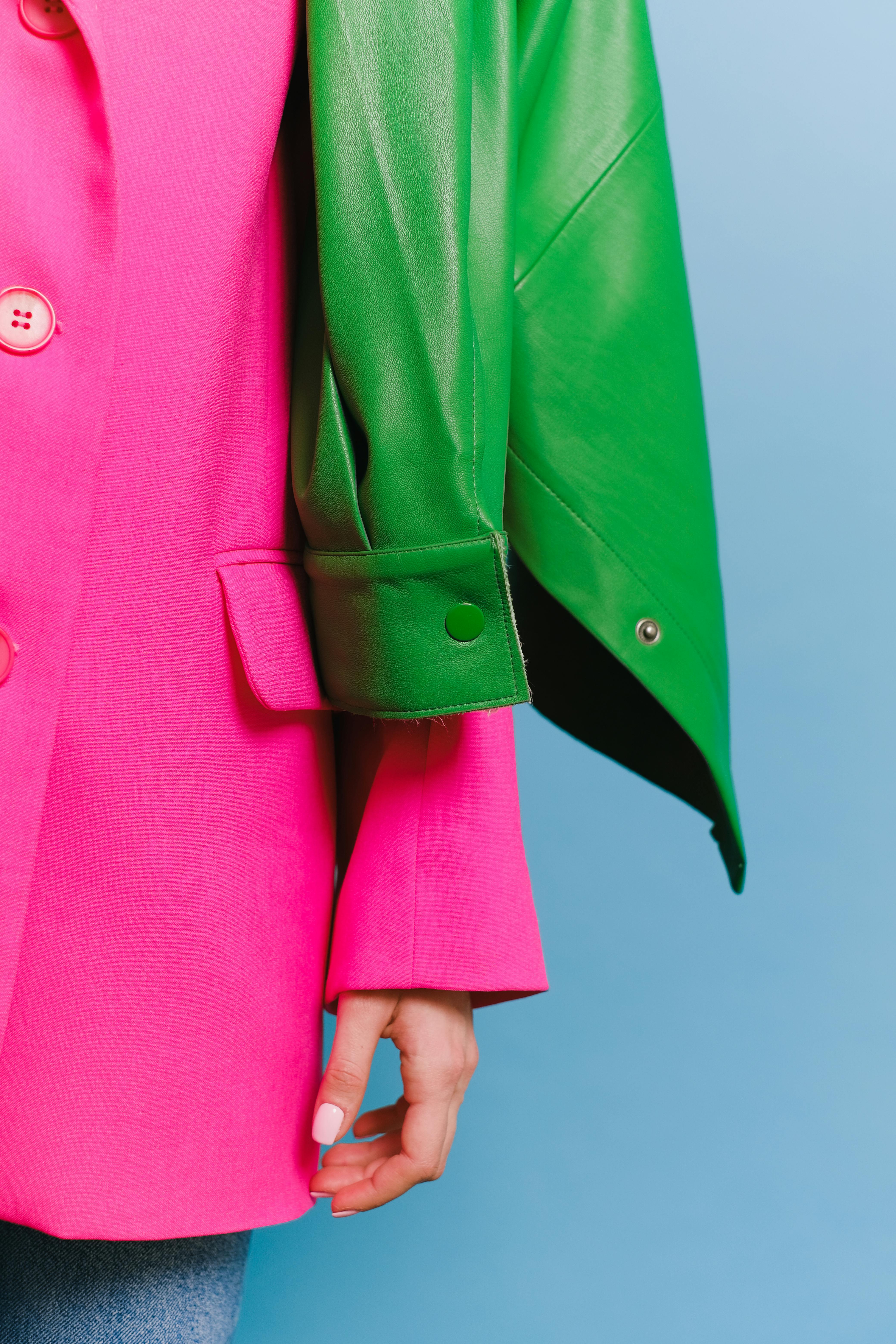 Image of a womans arm in a fun pink blazer with a green leather jacket 